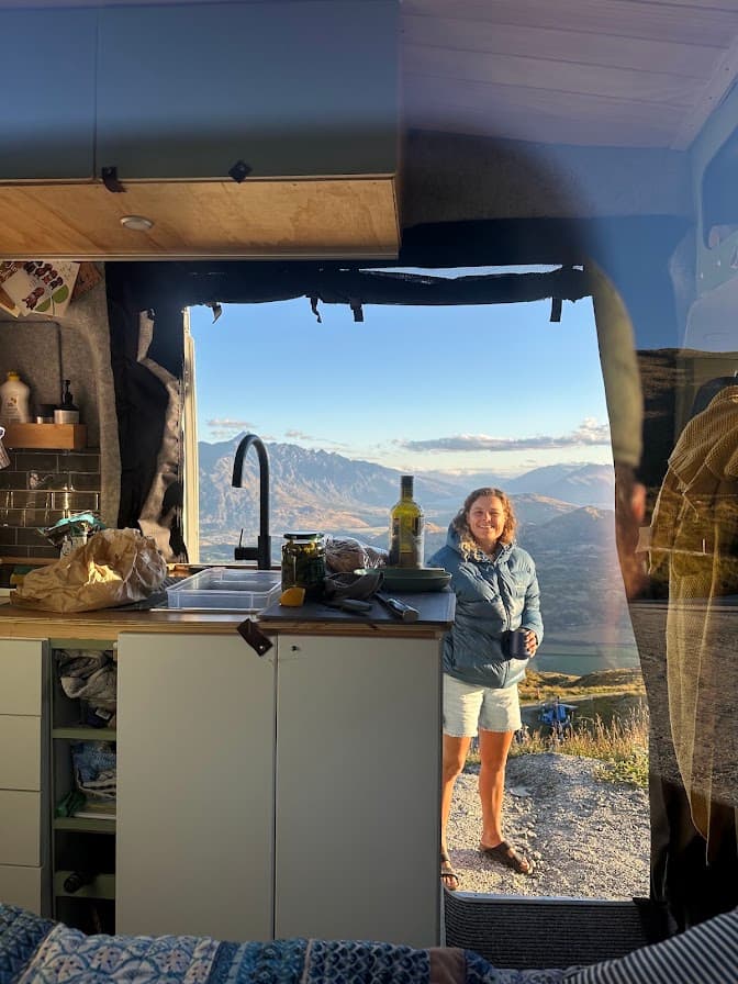 Issy in the doorway of the campervan's off-grid kitchen, mountains stretching out behind