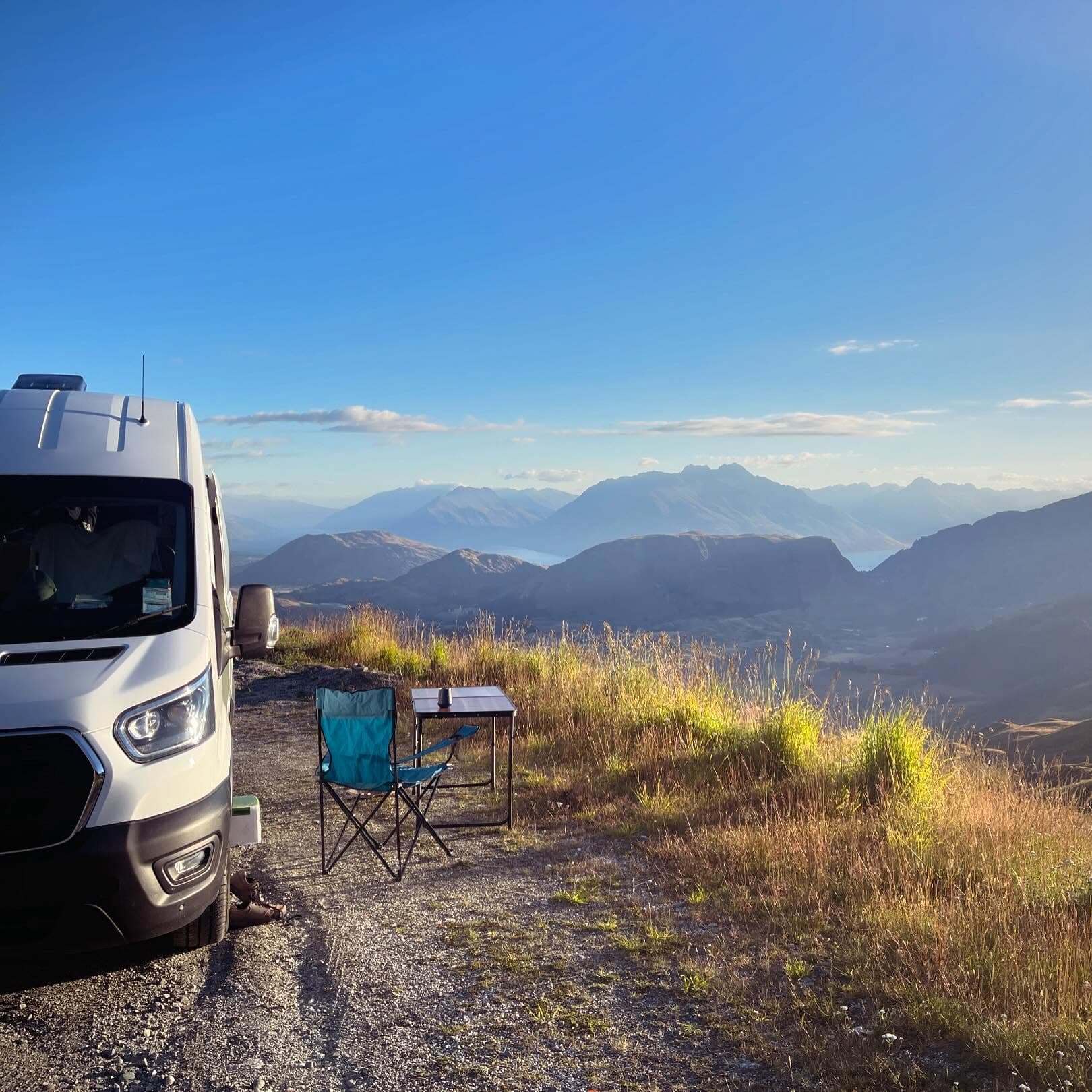 Mary, the off-grid campervan, parked on a hilltop above a New Zealand lake with camp chairs set out at golden hour