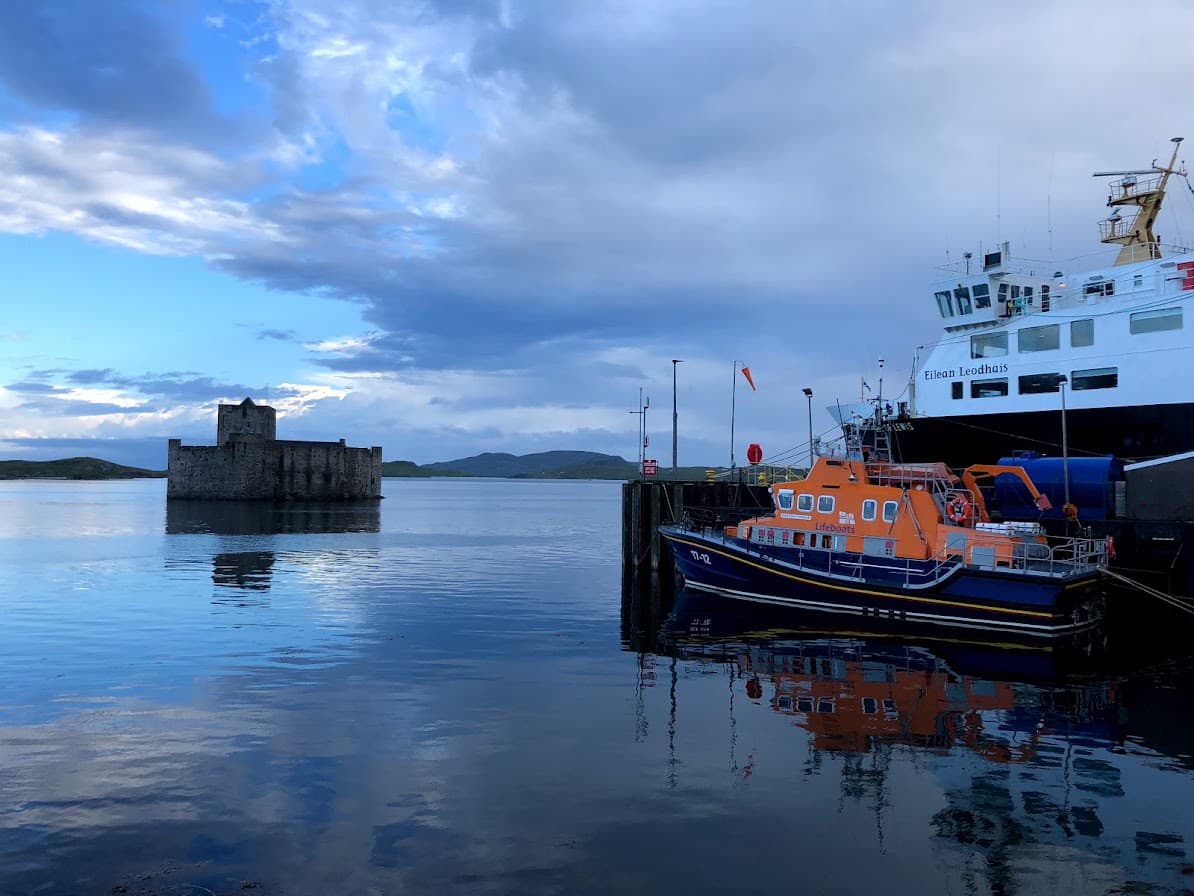 Kisimul Castle sitting in the sea at dusk, with a lifeboat and ferry moored nearby